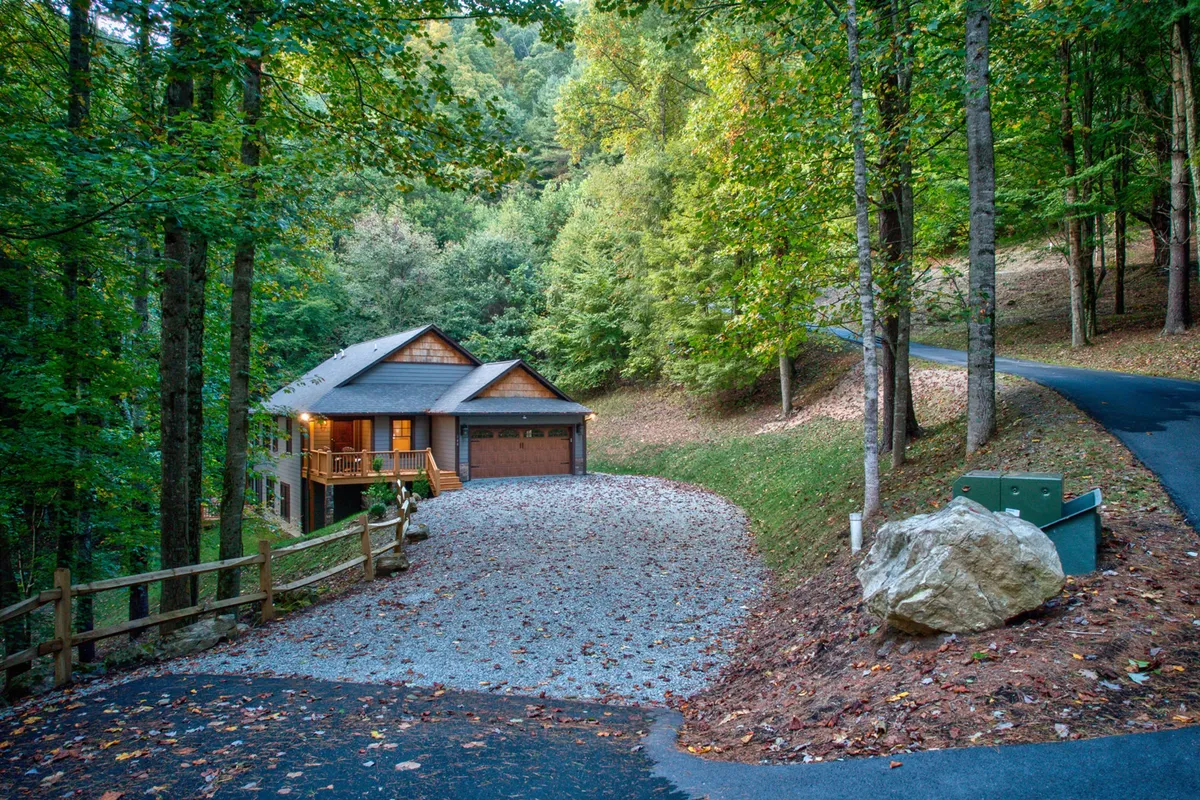 An exterior view of the retreat nestled among tall trees, with the house, driveway, rock formations, and surrounding natural beauty in view. The setting is peaceful and private, ideal for relaxation and exploration.