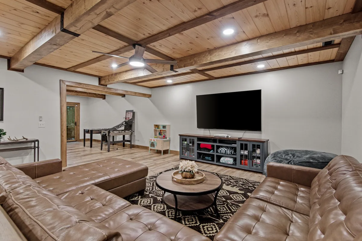 A spacious family room on the lower level with a large sectional sofa, a coffee table for board games, a television for movie nights, and a dedicated game table. The space is open and welcoming, inviting families to relax or compete in friendly games.
