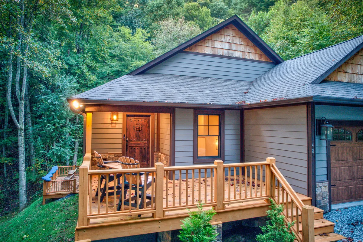 The image shows the inviting front porch of the retreat with a wooden railing and doorway, set against a natural backdrop. The porch is designed for relaxation, social gatherings, and soaking in the fresh mountain air.
